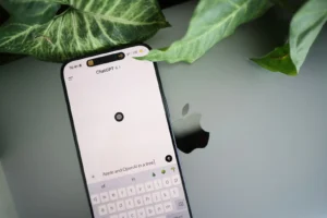 Interface ChatGPT sur smartphone posé sur un ordinateur portable Apple dans un environnement feuillu.