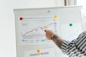 Personne tatouée pointant des graphiques financiers sur un tableau blanc.