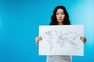Jeune femme tenant une carte du monde devant un fond bleu vif.